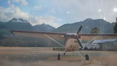 Small airplane parked on runway with mountains in background, sunlight animation