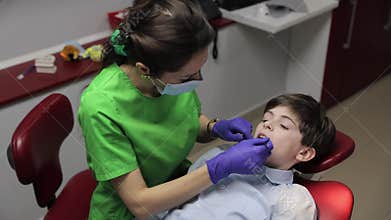 Cute positive boy in dental chair during caries treatment.