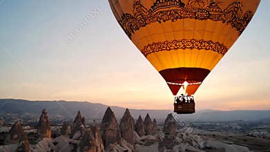 Orange hot air balloon with ornamental design floats over mountainous landscape at sunrise
