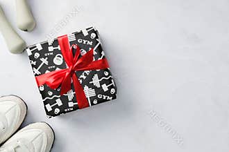 Fitness holiday gift box with sneakers and dumbbells on marble background.