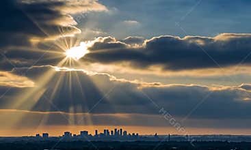 Spectacular sunset over the city skyline with sunbeams shining through the clouds.