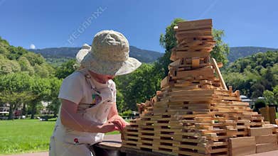 A focused smart little girl builds the big tower with toy wooden blocks