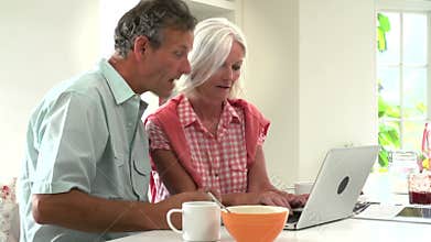 Middle Aged Couple Looking At Laptop Over Breakfast