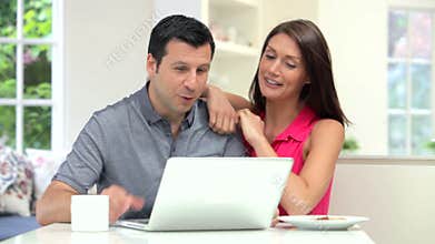 Hispanic Couple Looking At Laptop Whilst Eating Breakfast