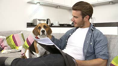 Man Looking At Paperwork And Playing With Pet Dog At Home