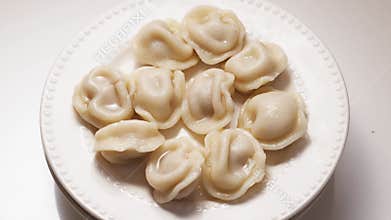 Boiled dumplings with dill are arranged in a circle on a white plate.