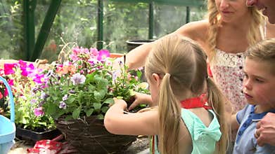 Family Planting Hanging Basket In Greenhouse