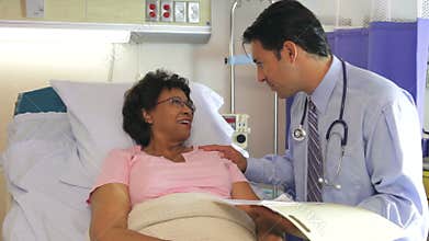 Doctor Talking To Senior Female Patient In Hospital Bed