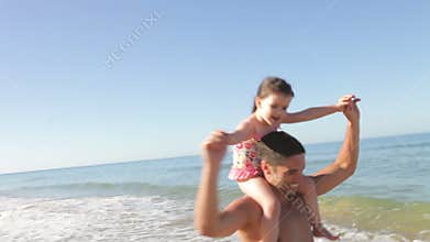 Father Running Along Beach Carrying Daughter On Shoulders