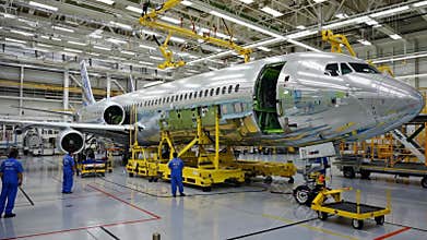 Aircraft assembly plant with workers in blue uniforms constructing a large commercial airplane, surrounded by advanced