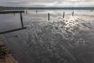 Weird cloud reflections in the calm water of a lake surrounded by trees.