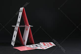 House of playing cards on black background, space for text
