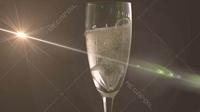 Horizontal beam glancing off champagne flute illuminating bubbles creating green flare artifacts