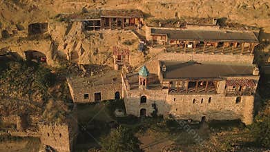 Aerial view of Orthodox monk chat talk with visitor on staircase in remote cave monastery complex carved into cliffs, symbolizing