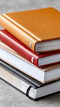Four hardcover books in vibrant colors are stacked together, showcasing their textures against a gray background