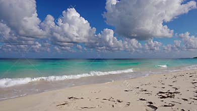Gentle waves are washing the white sand beach on a sunny day, with turquoise water and a beautiful cloudscape creating a perfect