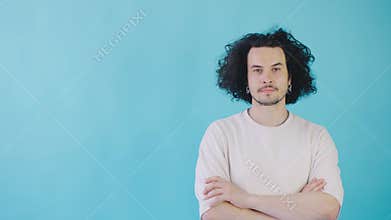 In a minimalist studio, a confident young man with curly hair exudes calm and contemporary vibes in a white sweater
