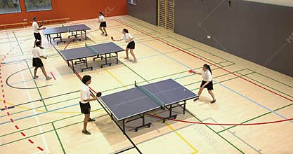 Playing table tennis in school gym, students practicing and competing in pairs