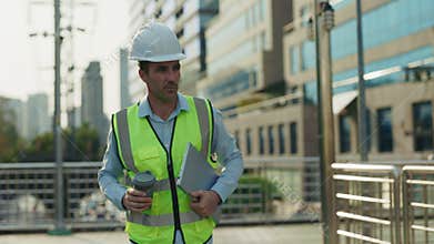 Man engineer walks on footbridge holding cup of coffee and laptop