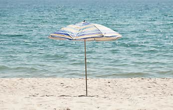 Striped beach umbrella standing on white sand, isolated against a white background