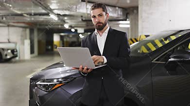 Caucasian businessman using laptop beside car in parking garage