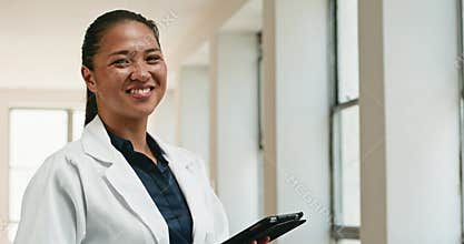 Confident Young Doctor Smiles in Hospital Corridor with Digital Tablet, Exuding Competence and Care