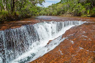 A waterfall in the tropical rainforest cascades into a fissure in its riverbed.