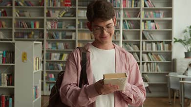 Teenage guy smiling happy looking at camera holding book buying literature prepare for reading in books store library in
