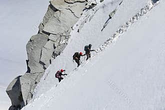 Three mountaineers climb a snowy mountain.