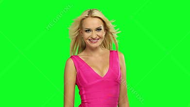 Attractive Caucasian blond woman wearing a pink dress, dancing, on fluorescent green background