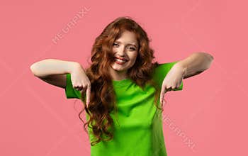 Charming woman pointing down advertising area. Pink background. Click subscribe