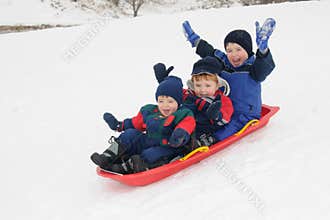 Three young boys sledding downhill together