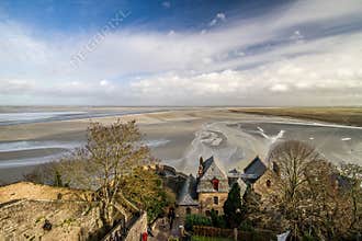 Elevated view of Mont Saint Michel showcasing its historic stone village, intricate architecture, and the vast, patterned tidal