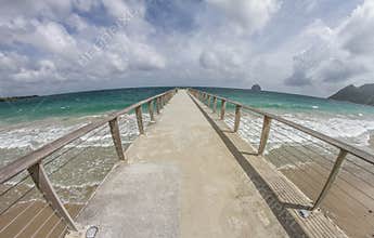 Wide-Angle Perspective of a Long Concrete Pier Stretching into the Turquoise Caribbean Sea under a Dynamic Cloudy Sky