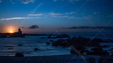Sunset over the sea near a lighthouse in Bretagne showing calm waters and rocky shoreline at dusk