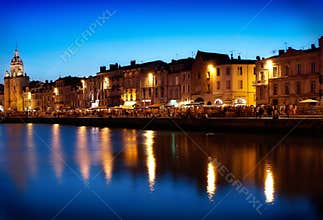 Historic La Rochelle Waterfront at Twilight: Illuminated Buildings and Clock Tower Reflecting in the Old Port's Calm Water,