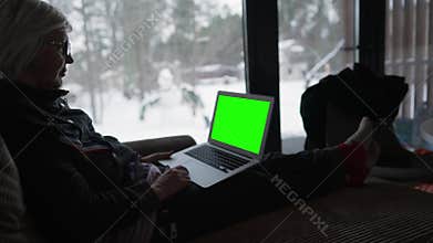 A woman in a house is browsing content on a laptop.