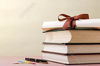 Books Stacked Together With Ribbon and Rolled Paper Beside Pen and Colorful Clips on Table