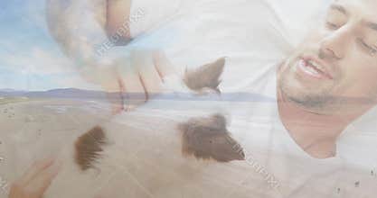 Reclining man wearing white tee overlaying beach on fabric with small brown-white dog, copy space