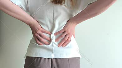 Woman grips her lower back with both hands suffering from