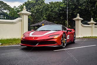 Red Ferrari SF90 stradale Plug-in Hybrid Electric Vehicle PHEV hypercar driving on the wet road after rain