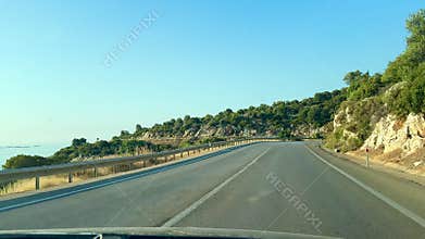 A winding road in Turkiye surrounded by rocky cliffs and sparse vegetation. A warning sign indicates a sharp turn ahead. Clear