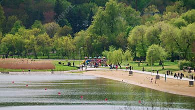 Wide shot of a public park with a playground, families, and a lakeside