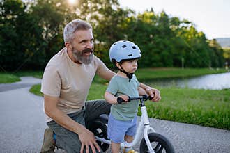 Father helping toddler son learn to ride balance bike for the first time.