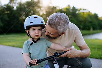 Father helping toddler son learn to ride balance bike for the first time.