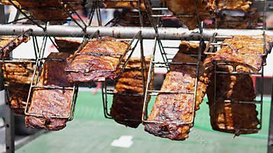 Marinated pork ribs hanging in wire baskets over outdoor grill