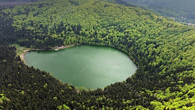Aerial drone view over a forested slope toward a round crater lake, La