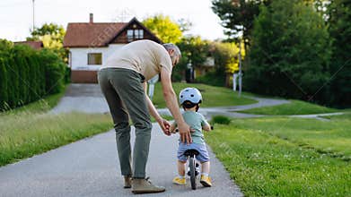 Father helping toddler son learn to ride balance bike for the first time.