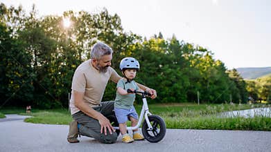 Father teaching toddler son to ride balance bike while wearing safety helmet.