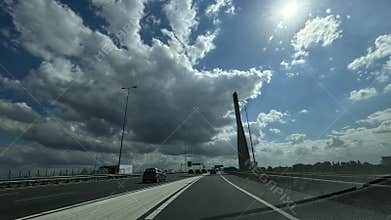 Dramatic highway bridge with moving traffic under towering clouds and bright